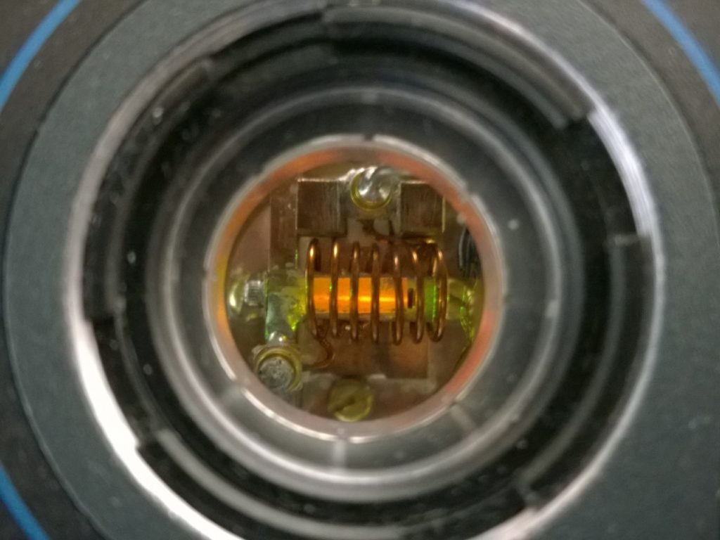 A europium-doped YSO crystal, of about 1 cm in length, as visibile from a window of our cryostat, while our yellow laser shines through it. The coil enveloping the crystal is used to address the spin states of europium via an oscillating magnetic field.